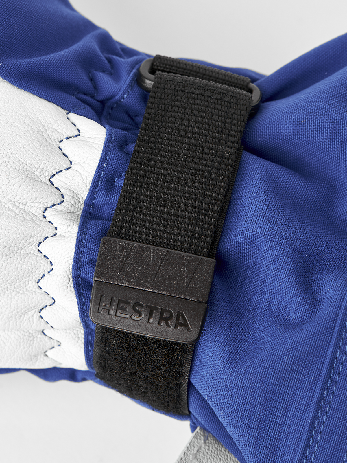 3-finger ski glove close-up with blue fabric, stitched trim, and HESTRA web strap.