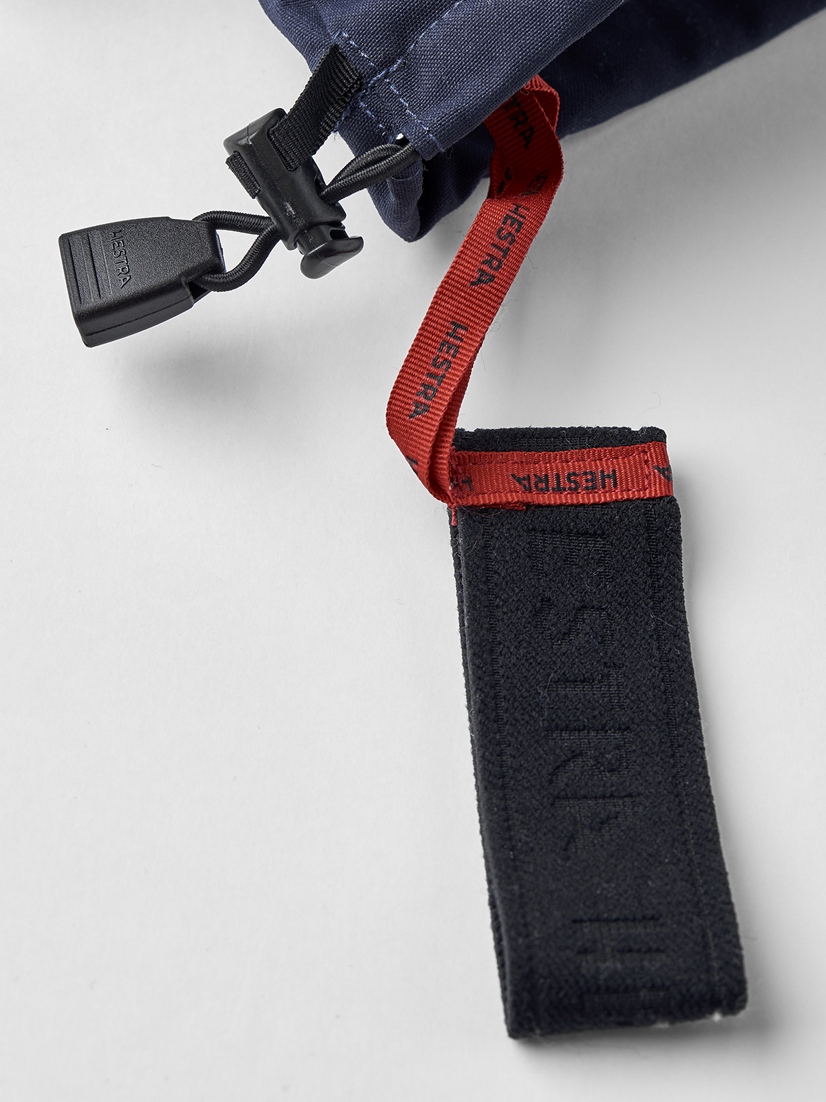 Ski glove cuff detail with red HESTRA webbing loop and dark fabric strap.
