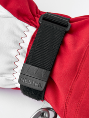 Red and white Hestra ski glove with black wrist strap and stitched cuff edge