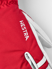 Red Hestra ski glove with white leather palm and vertical “Hestra” embroidery