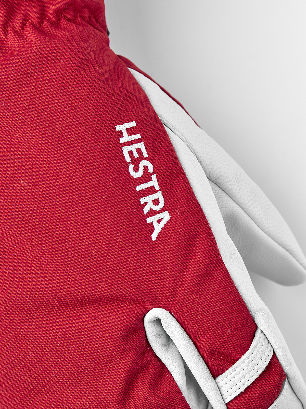 Red Hestra ski glove with white leather palm and vertical “Hestra” embroidery