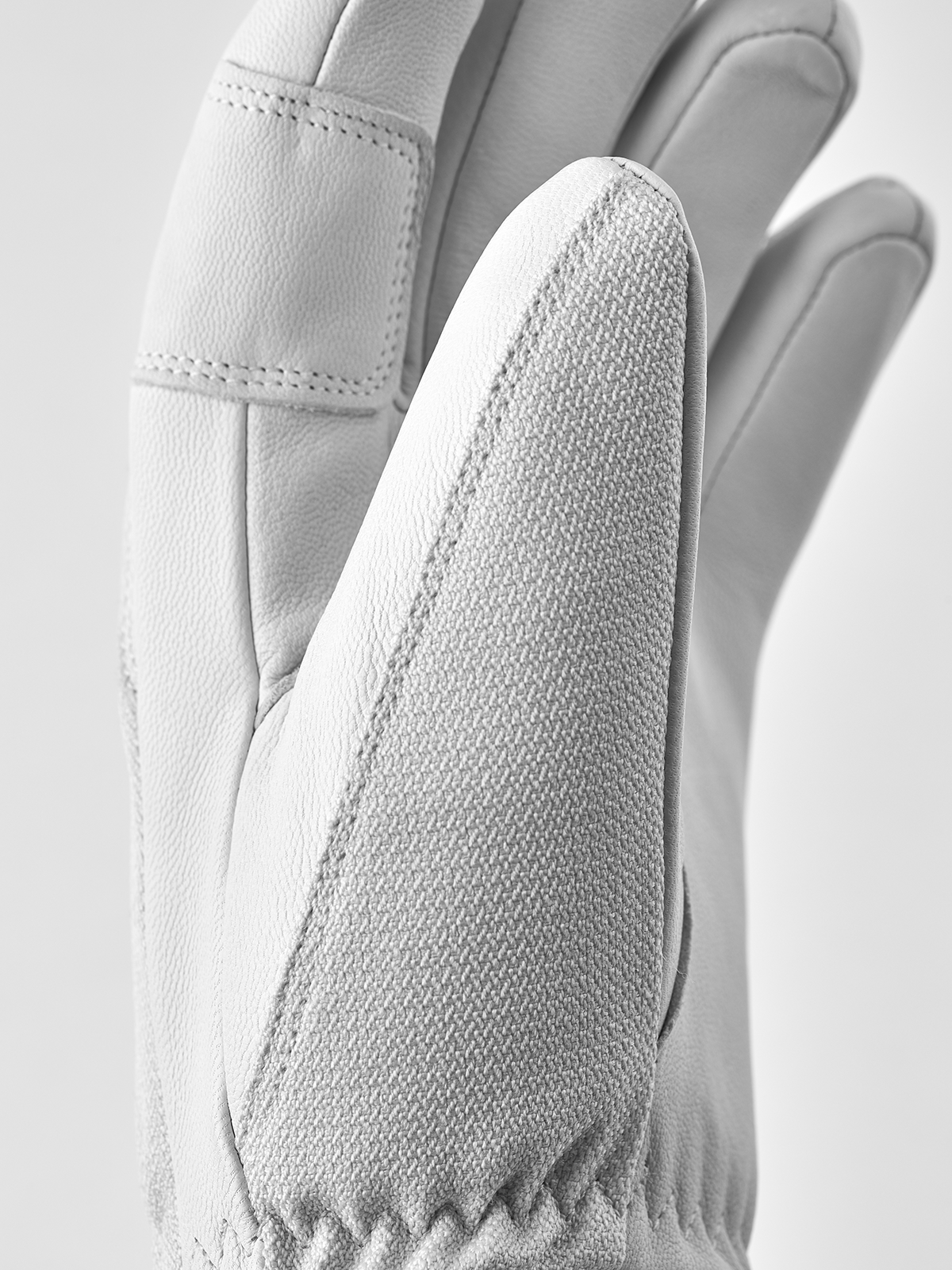 White leather patrol gloves with textured fabric side panel and stitched finger seams.