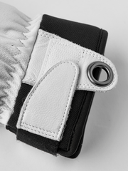 Close-up of black glove wrist strap with white leather patch and metal eyelet ring.