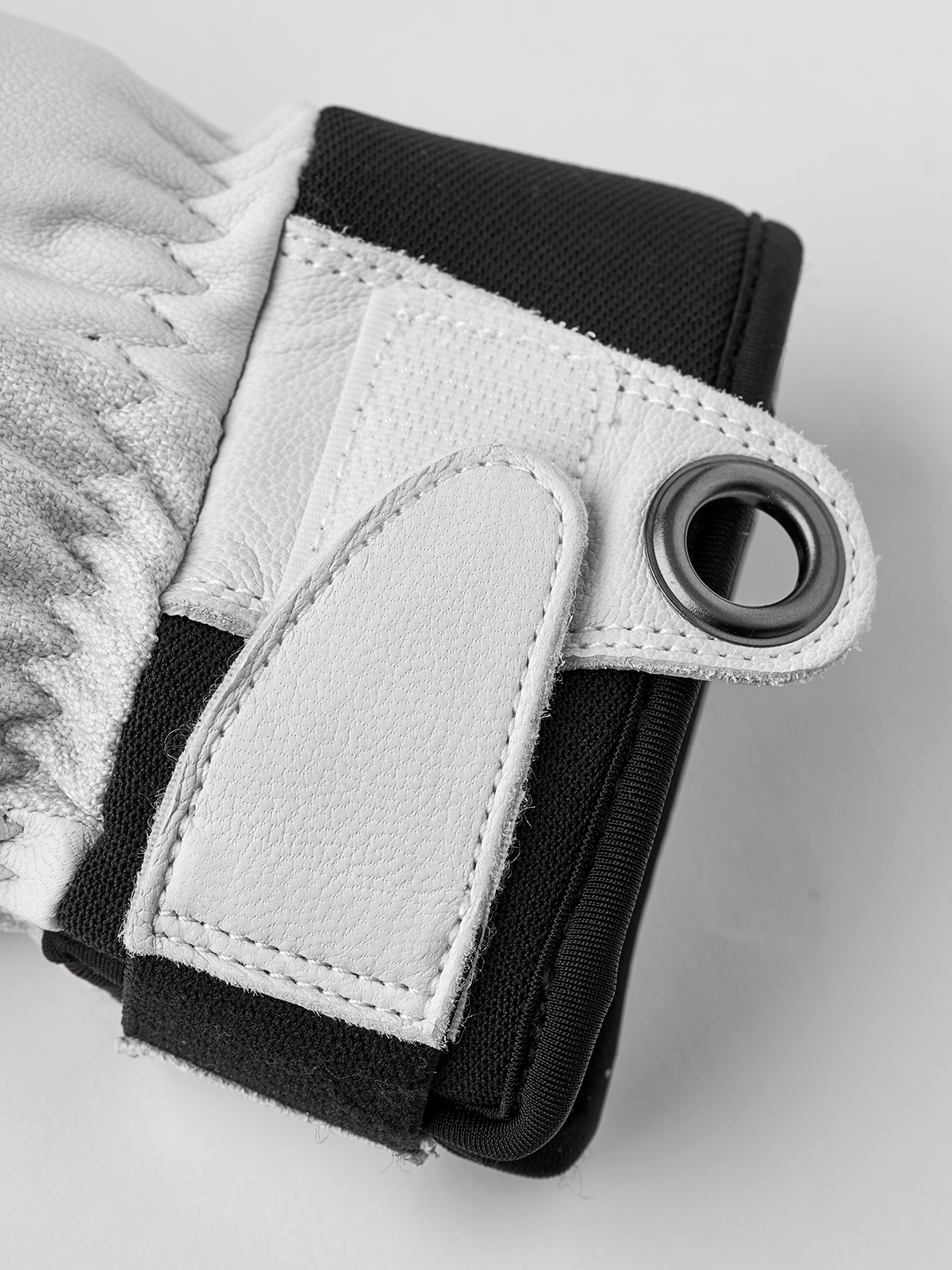 Close-up of black glove wrist strap with white leather patch and metal eyelet ring.