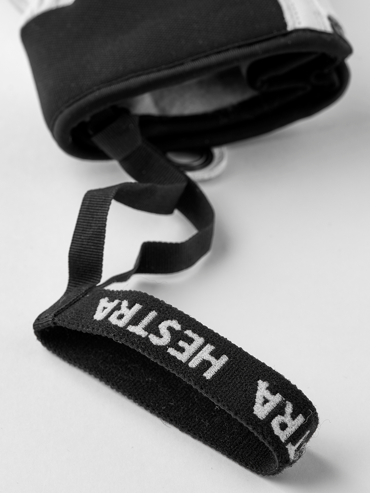 Black wrist strap with Hestra logo on a light glove cuff and metal eyelet