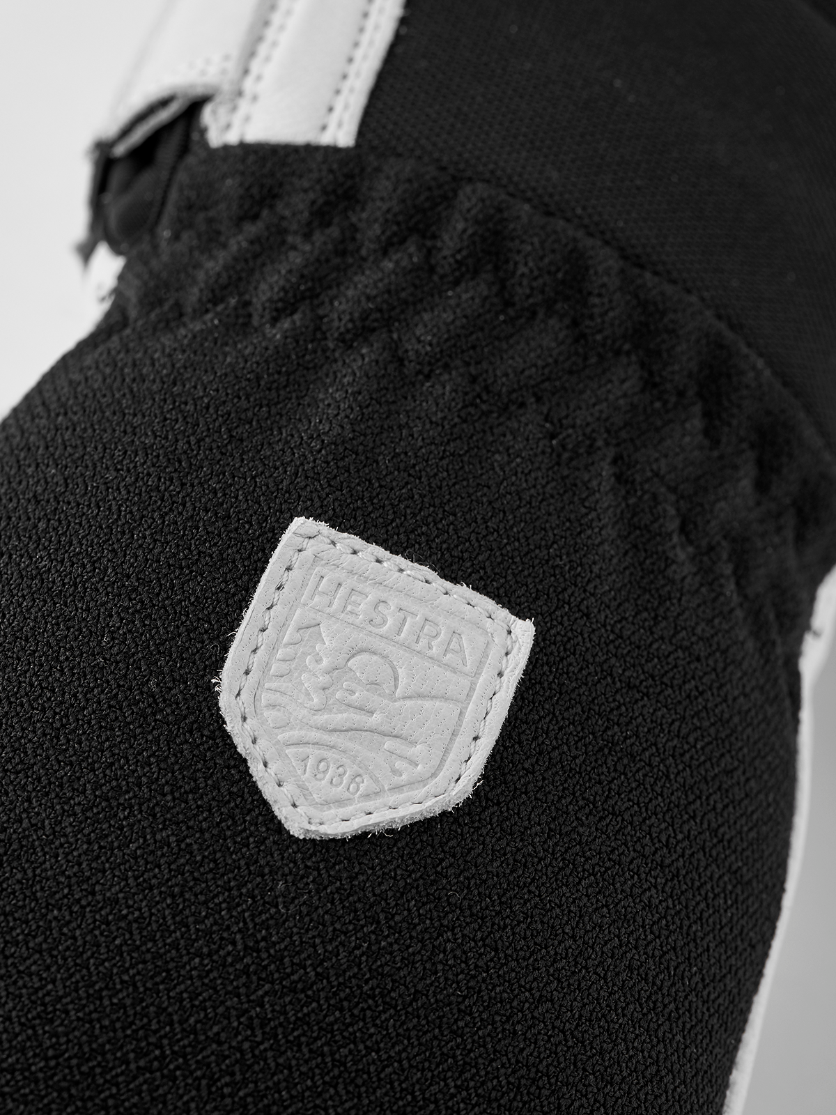 Dark glove with textured fabric cuff and Hestra shield logo patch
