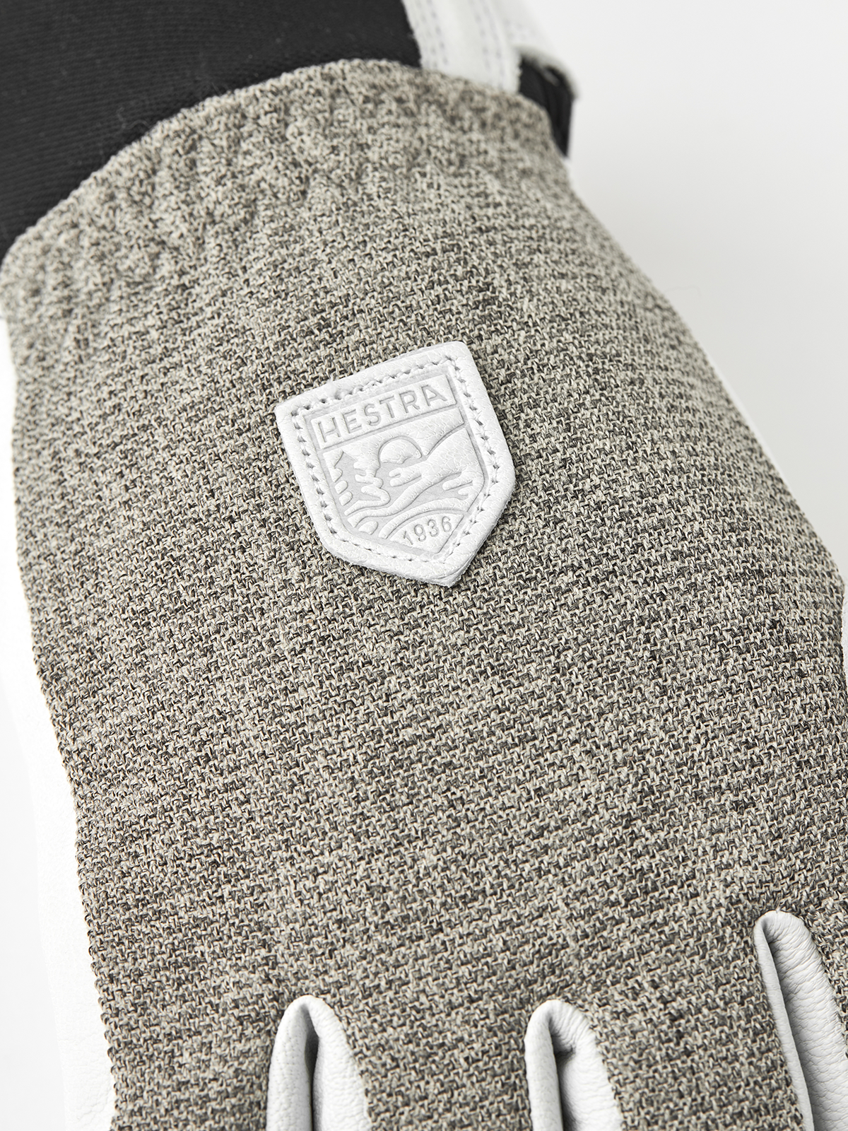 Close-up of textured gray fabric patrol glove with leather brand patch and white cuffs.