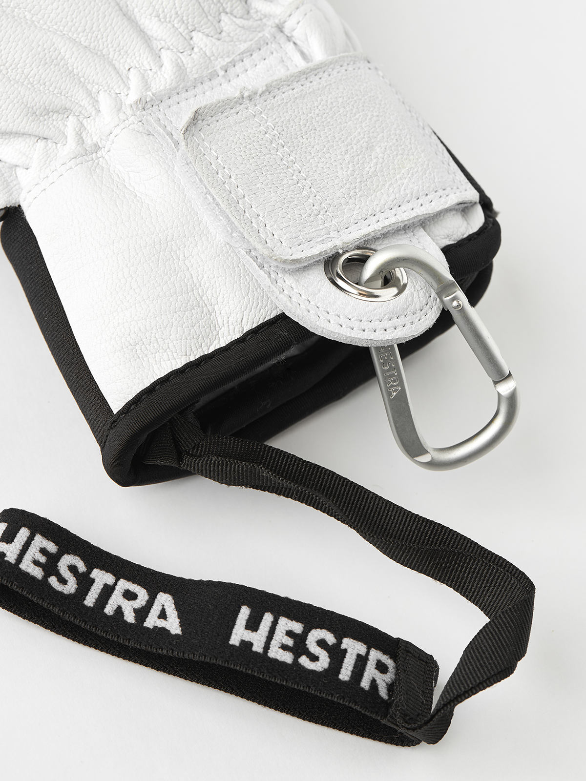 White leather glove with black strap and metal ring/clip at wrist.