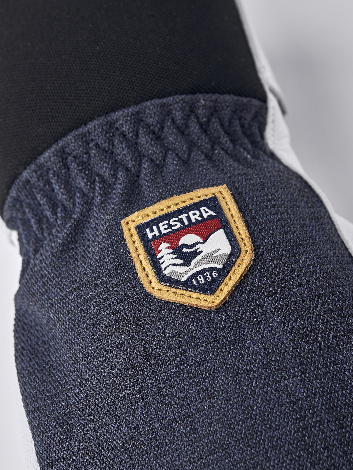 Navy textured glove with tan-bordered Hestra patch.