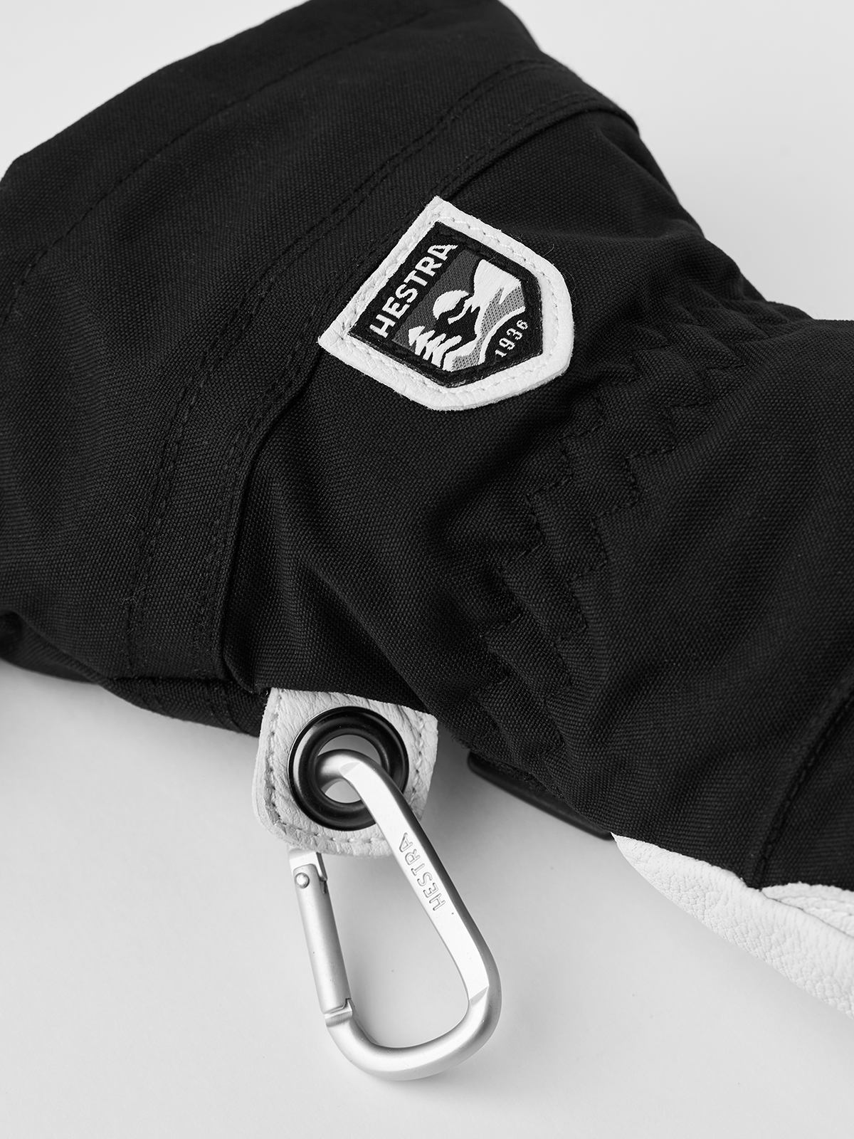 Black Hestra ski glove close-up with logo patch and metal carabiner clip