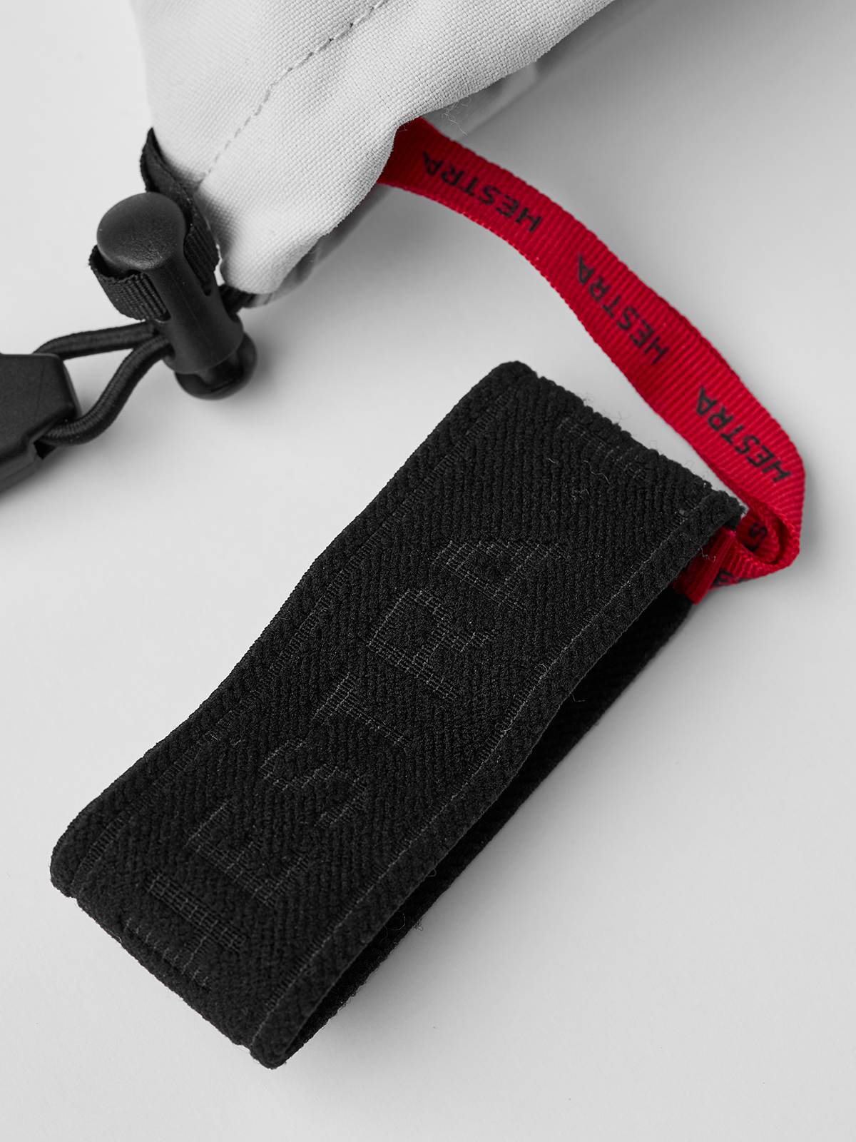 Off-white ski glove with black textured strap and red pull tab detail