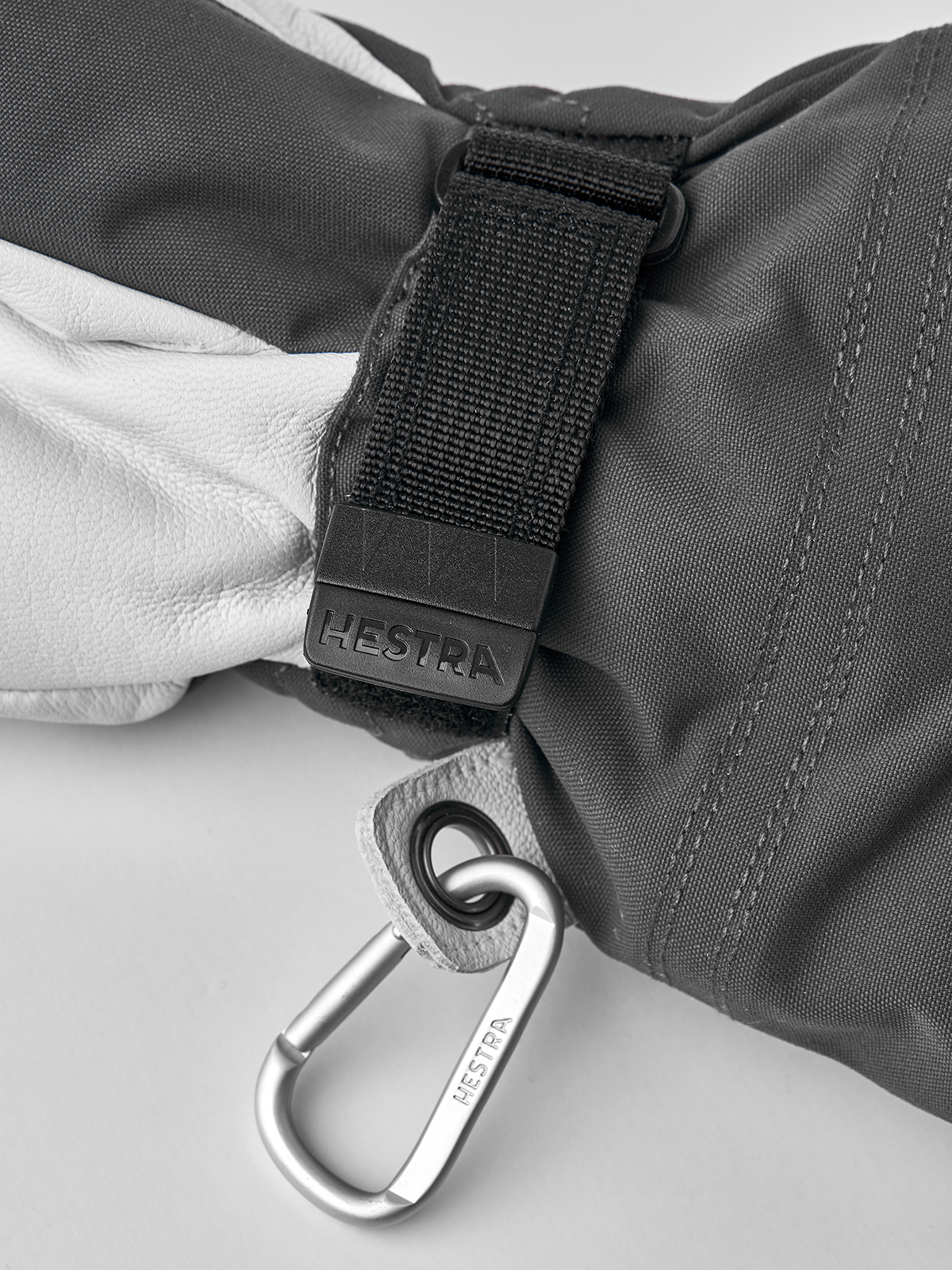 Gray ski glove close-up with woven wrist strap and metal carabiner clip