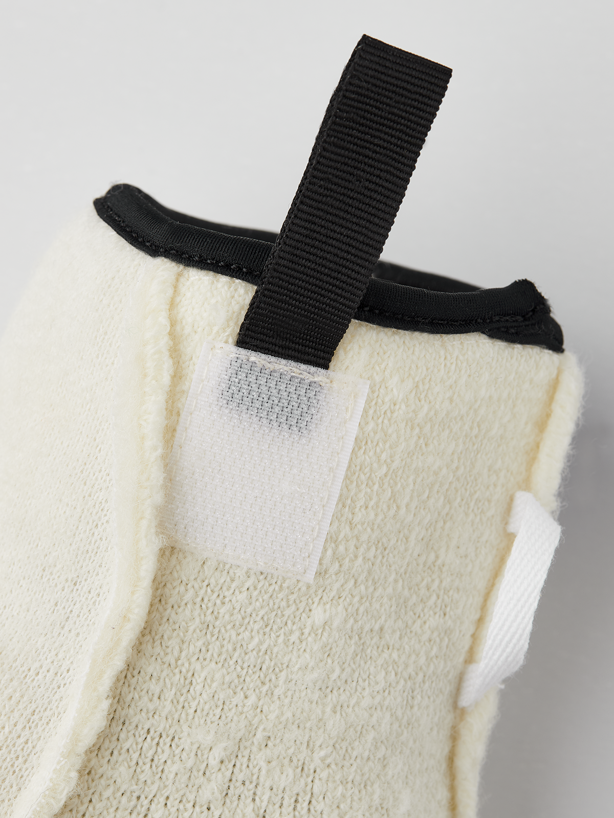 Off-white wool glove liner with black strap and stitched pocket detail
