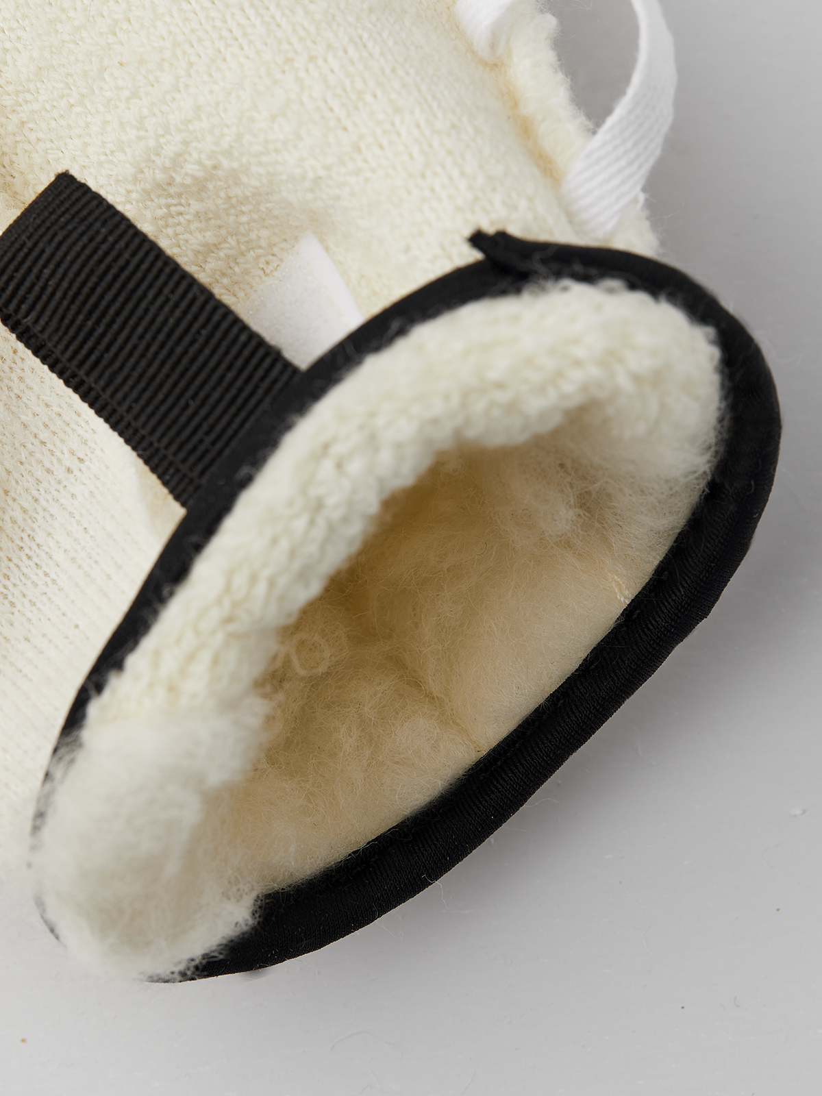 Close-up of off-white glove liner with black elastic strap and terry-pile interior
