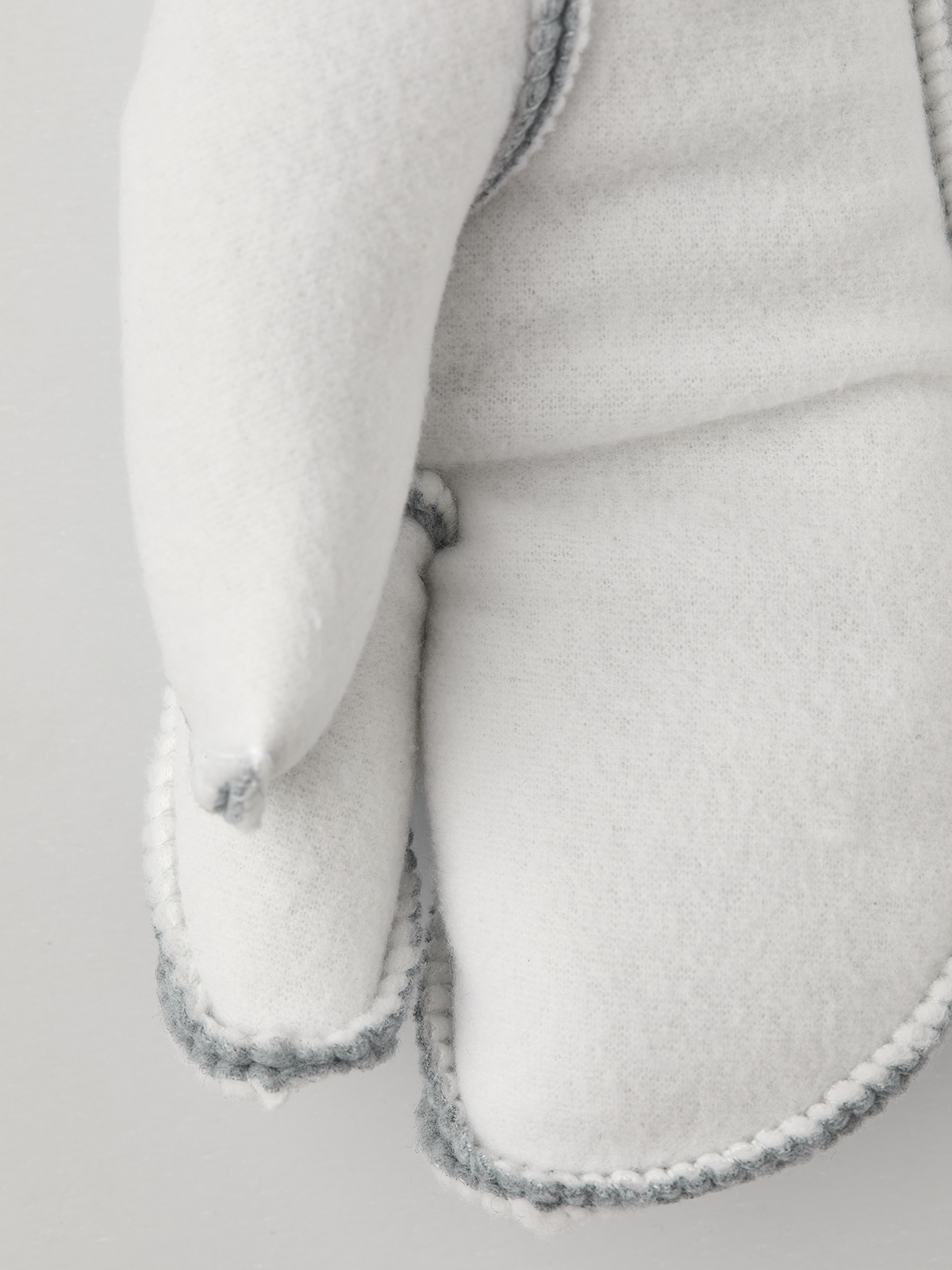 Off-white 3-finger ski glove liners, close-up cuff seam with light blue stitching
