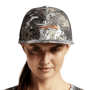 Camouflage women's trucker cap on model, black mesh sides and orange antler logo
