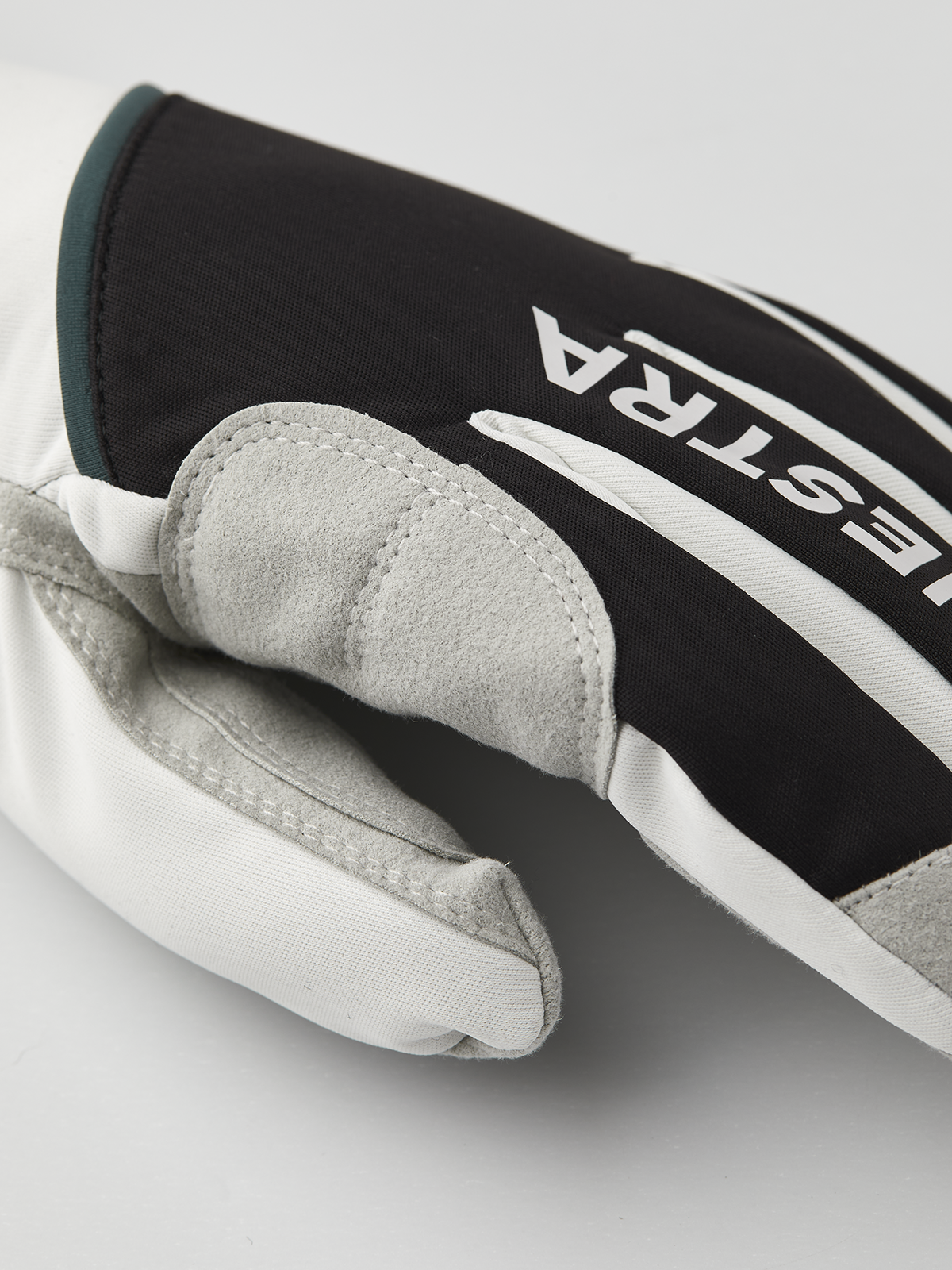 Black and off-white glove close-up with gray suede fingertips and Hestra branding