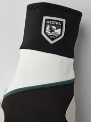 Black and off-white winter gloves with Hestra shield patch and teal accent band