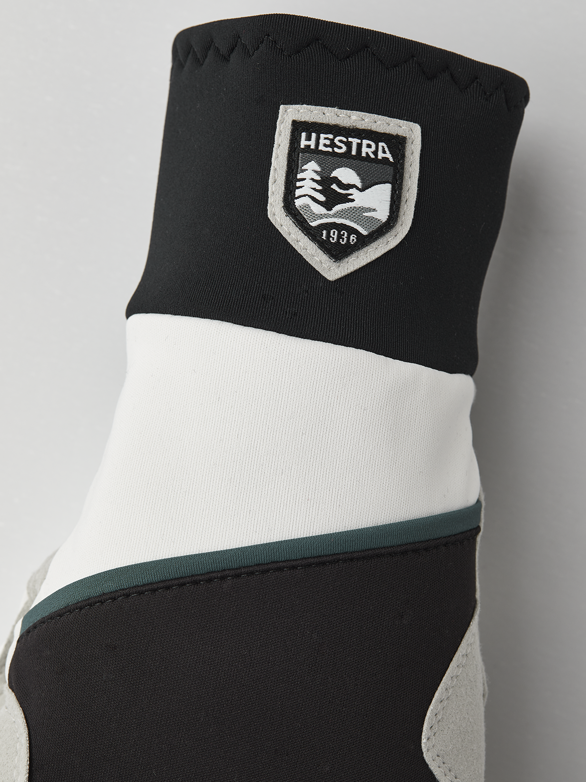 Black and off-white winter gloves with Hestra shield patch and teal accent band