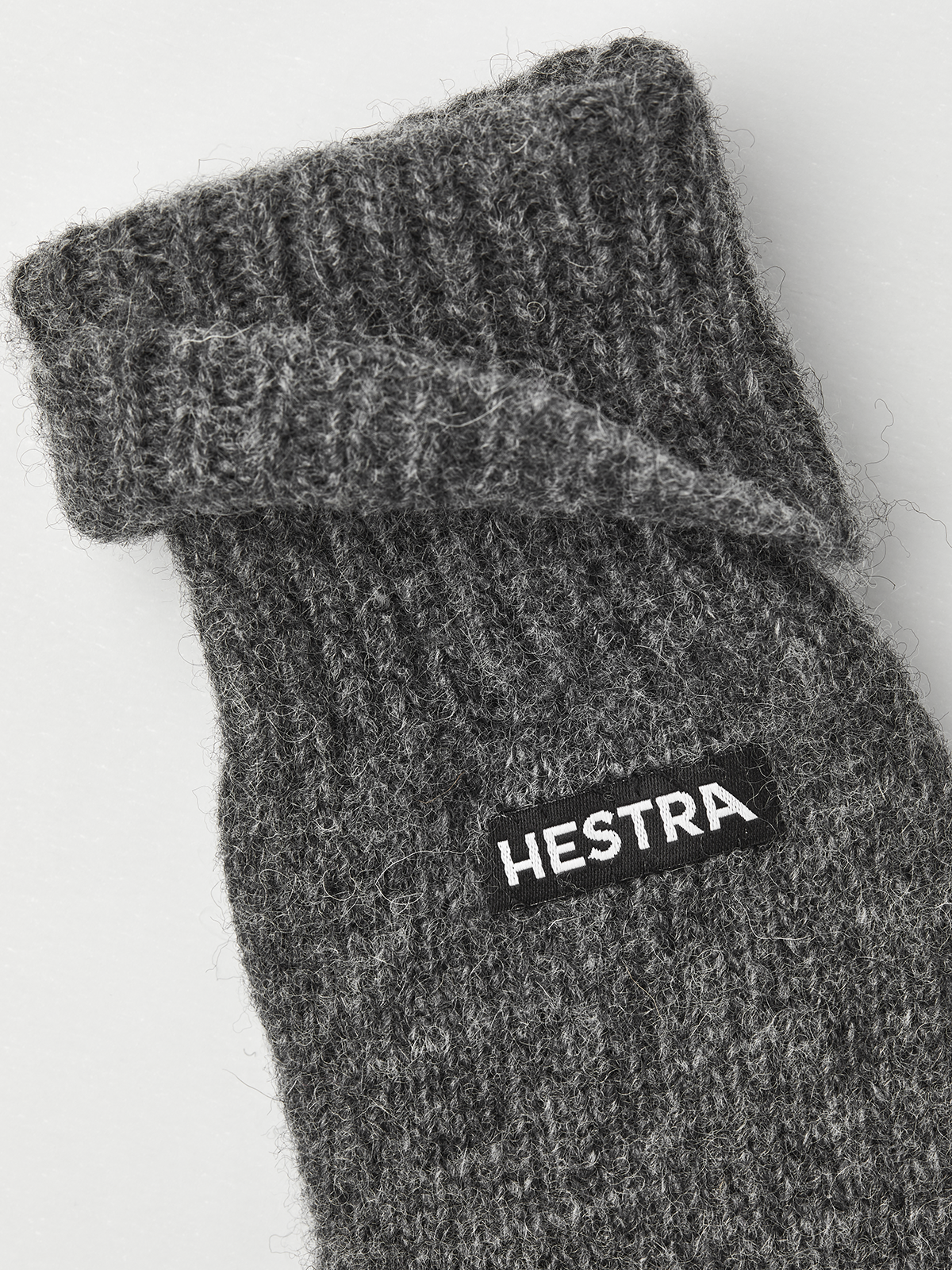 Grey knit glove liner close-up with Hestra logo patch on cuff