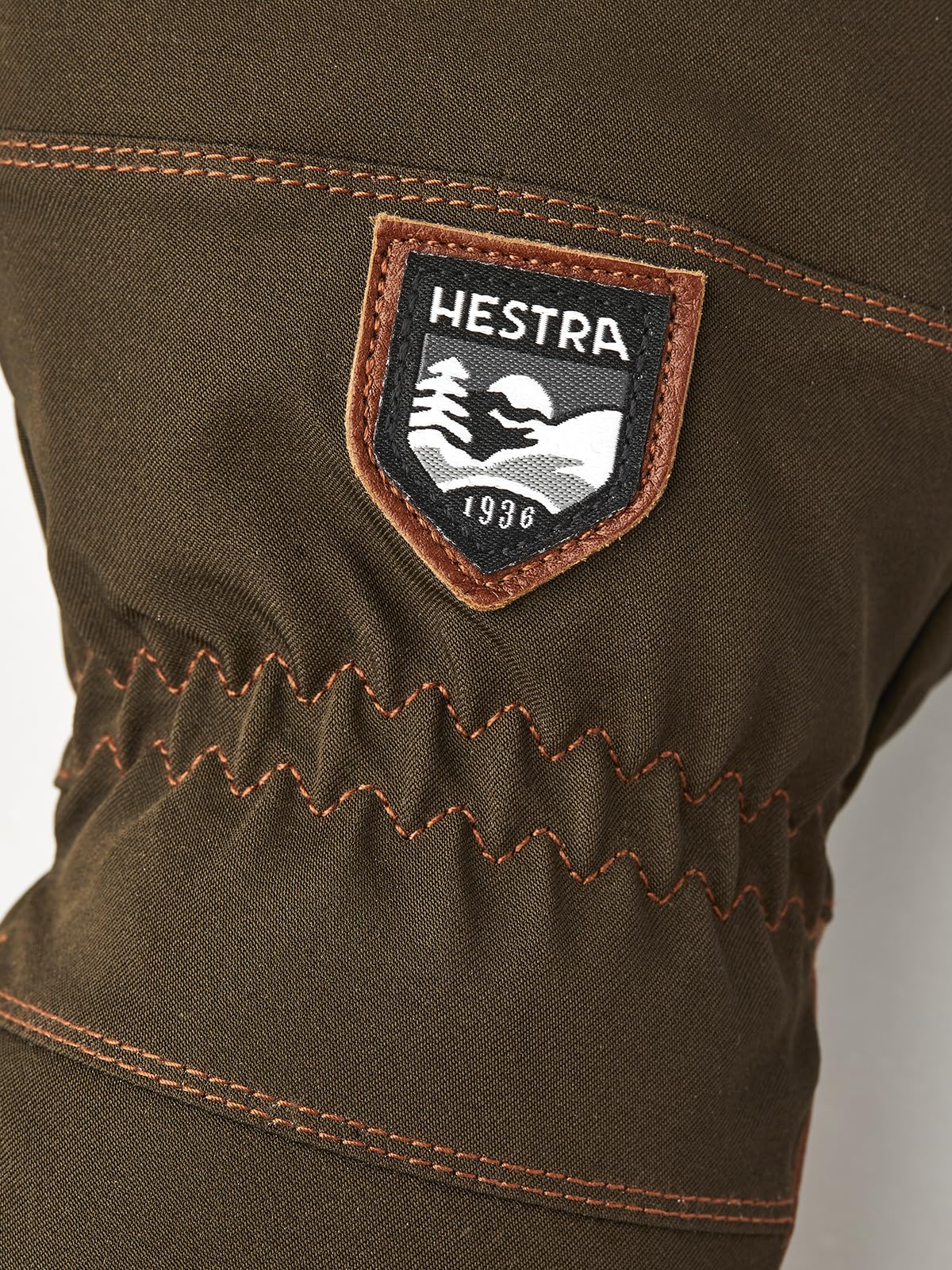 Hestra patch on dark olive glove with orange stitching and zigzag reinforced seam.