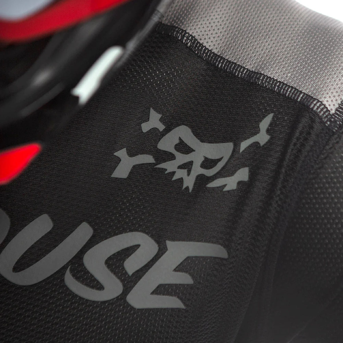 Black mesh jersey shoulder close-up with gray logo graphic and stitched trim