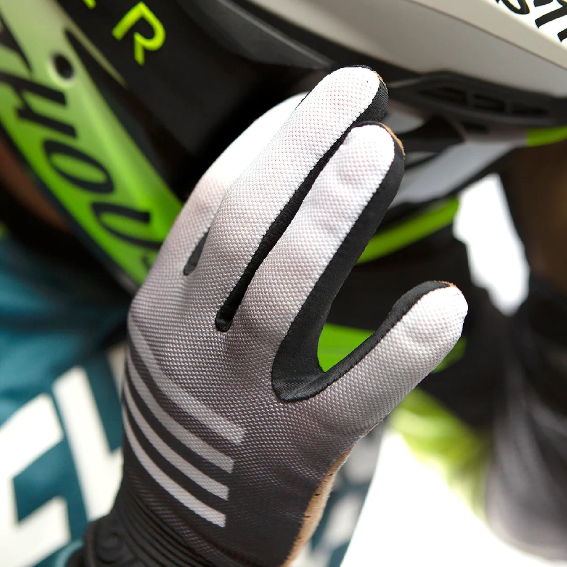 Gray cycling glove with white stripe graphics and black cuff, gripping handlebar