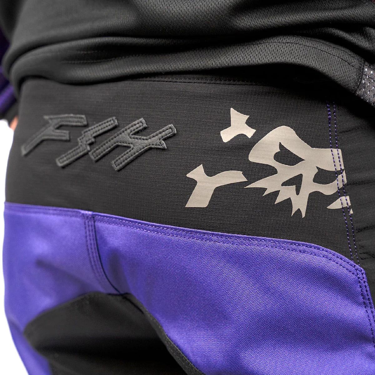 Black riding pants with “Fasthouse” logo, skull graphic, and purple lower panel
