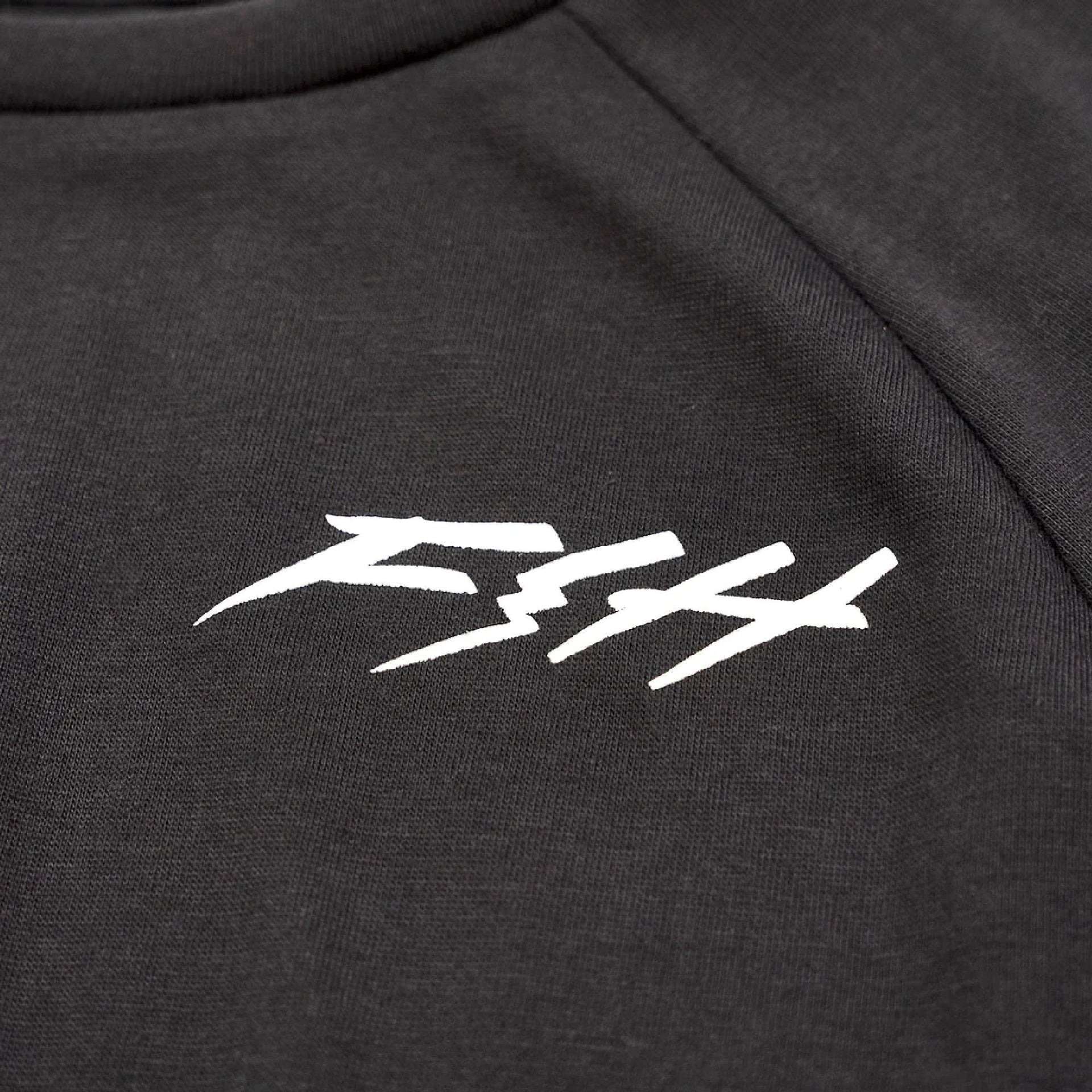 Close-up of white Fasthouse logo on black Fasthouse Rush raglan tech tee fabric