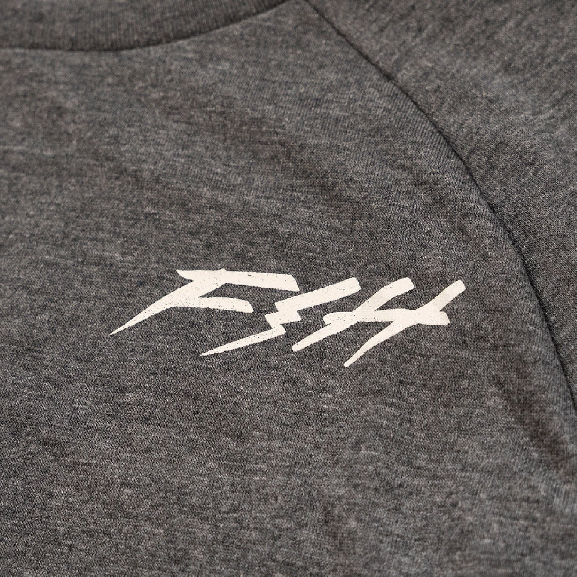 Close-up of white Fasthouse logo on heather gray Fasthouse Rush raglan tech tee fabric