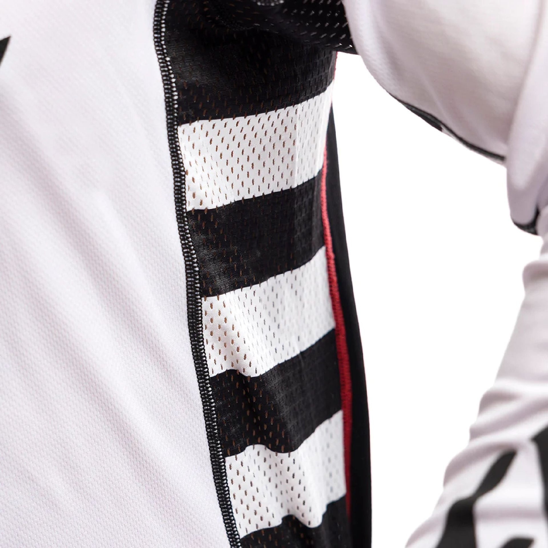 Motorcycle jersey side panel detail with white and black mesh stripes and red trim seam.