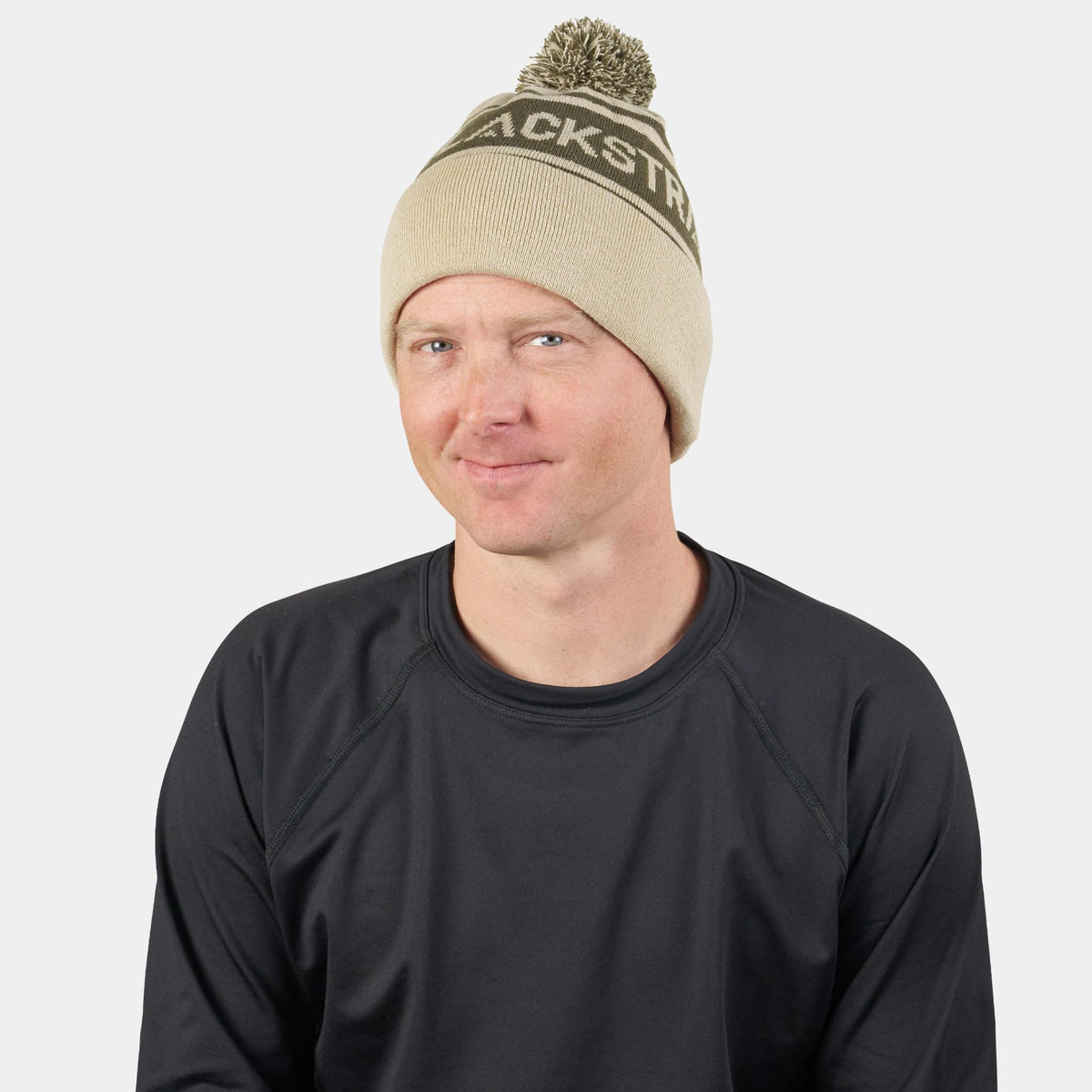 Oatmeal pom beanie with dark logo stripe; adult wearing the beanie