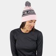 Pink pom beanie with black logo stripe; model wearing the beanie