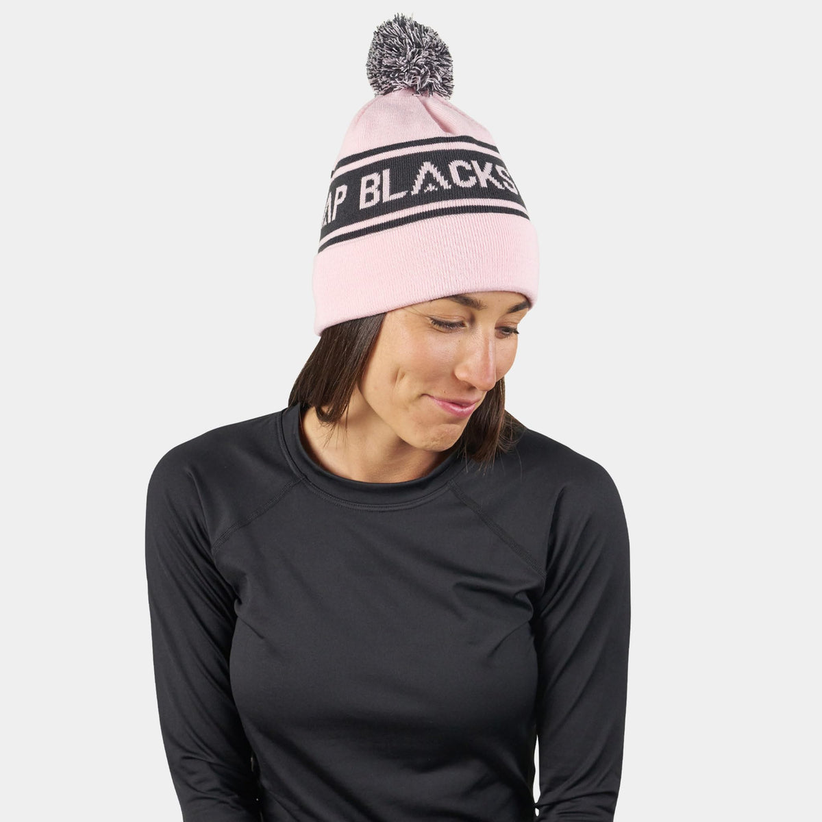 Pink pom beanie with black logo stripe; model wearing the beanie